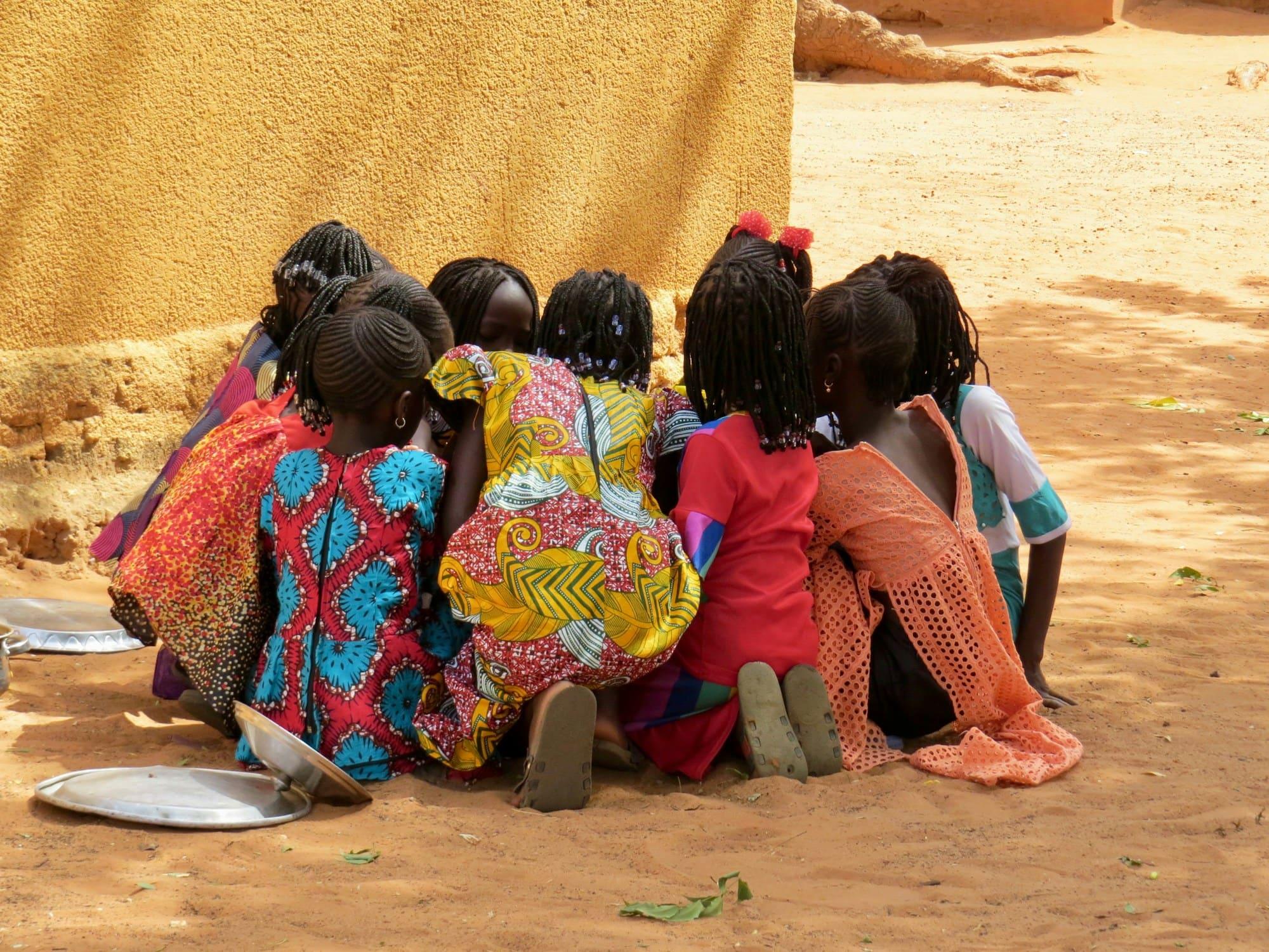 Young girls in colourful dresses huddle together outdoors