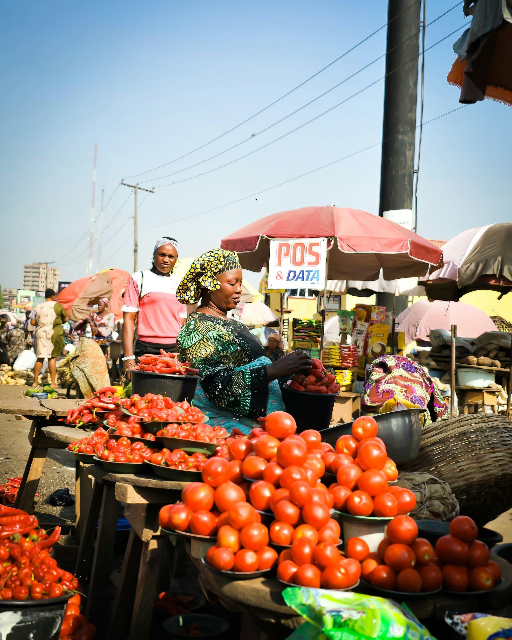 A trader arranges tomatoes at her busy market stall