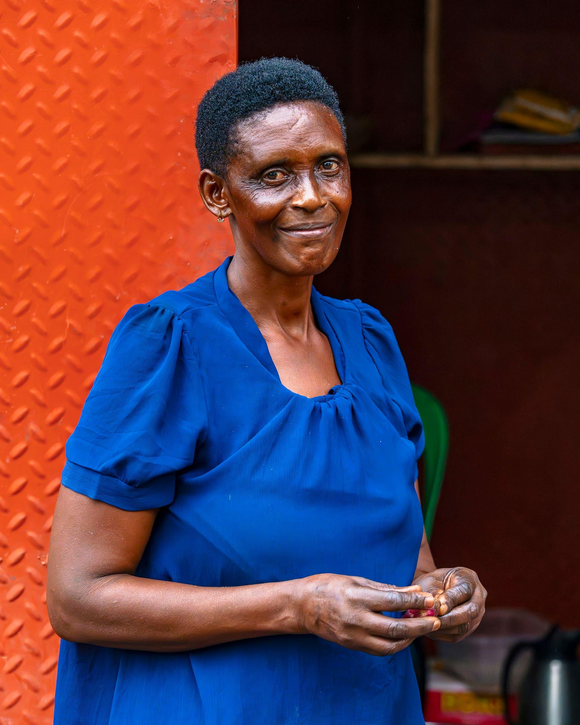 A woman in a blue dress smiles in front of an orange wall