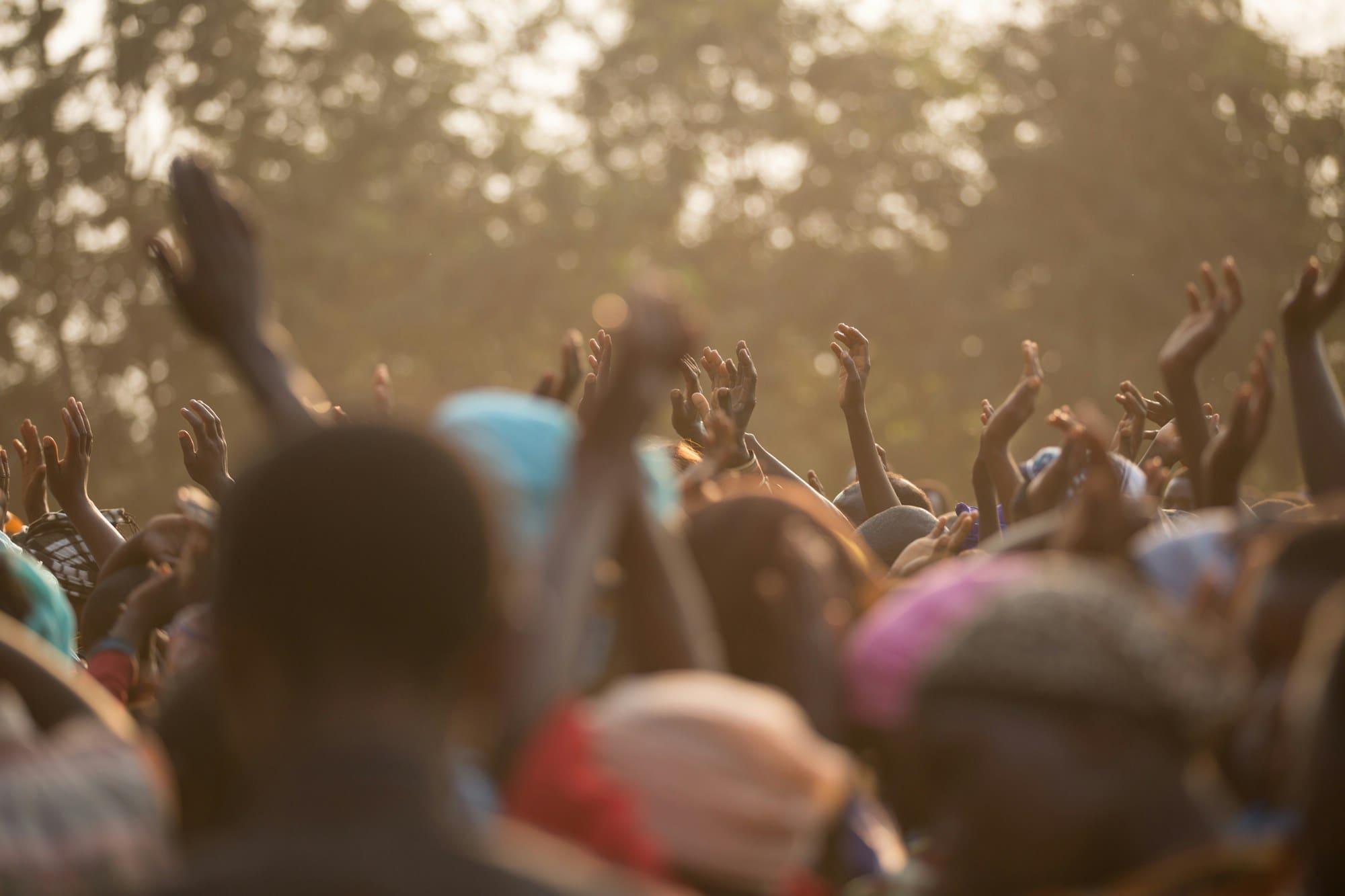 A crowd raises their hands in worship at an outdoor gathering